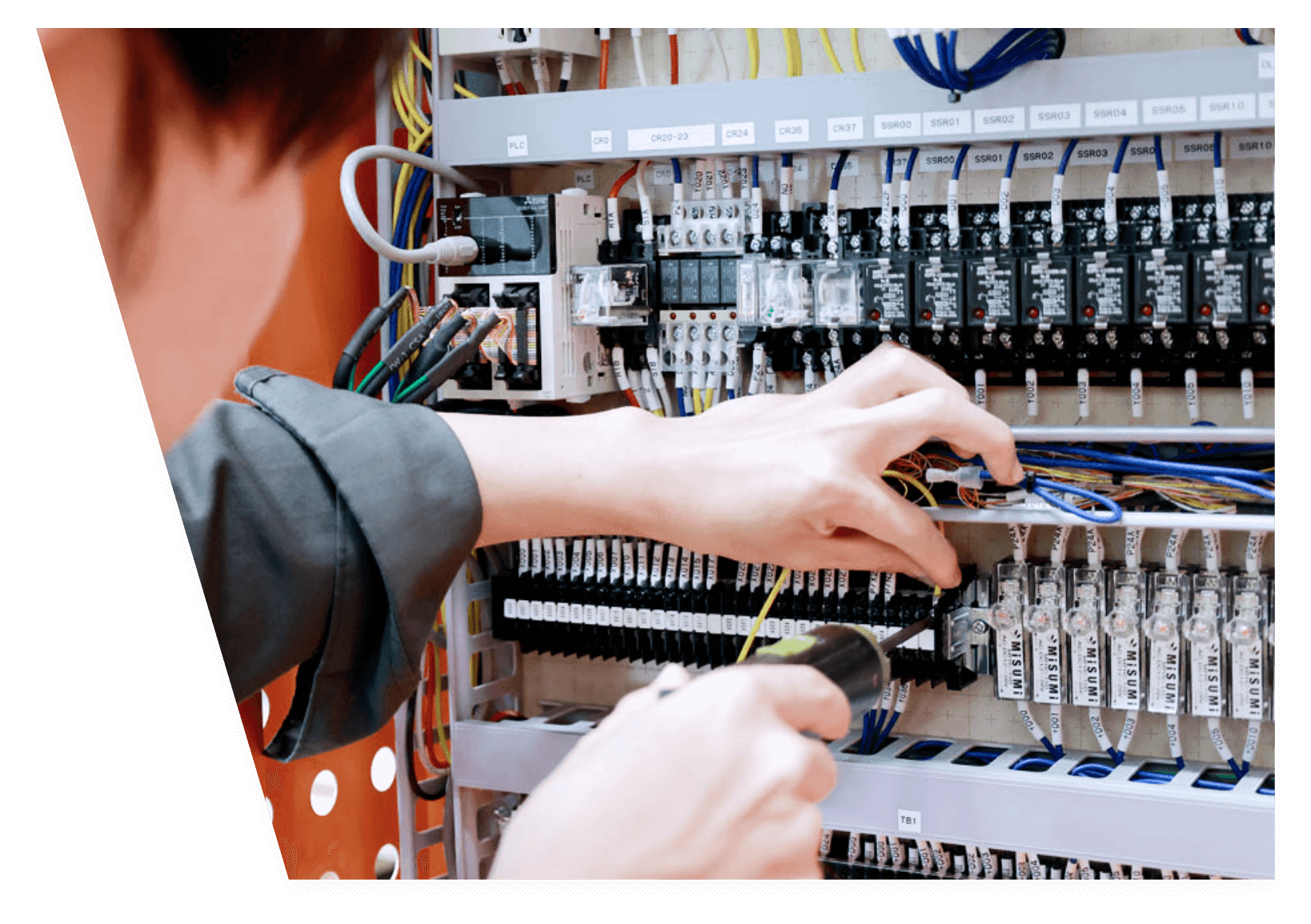 配線盤の内部で作業者がドライバーを使い、電線や端子を調整・接続している様子。
