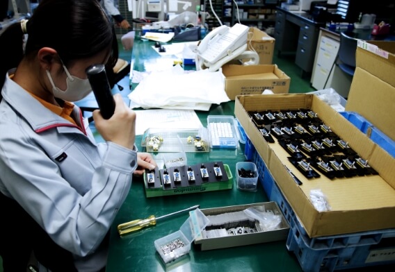 製造現場で部品の検査と加工が行われており、精密な作業風景が切り取られている