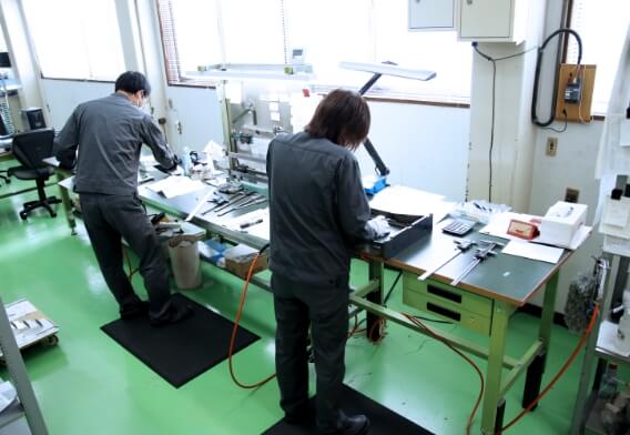製造現場で部品の検査と加工が行われており、精密な作業風景が切り取られている