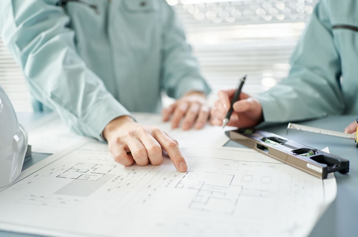作業着姿の社員が設計図を指し示しながら打ち合わせを行っている様子。
